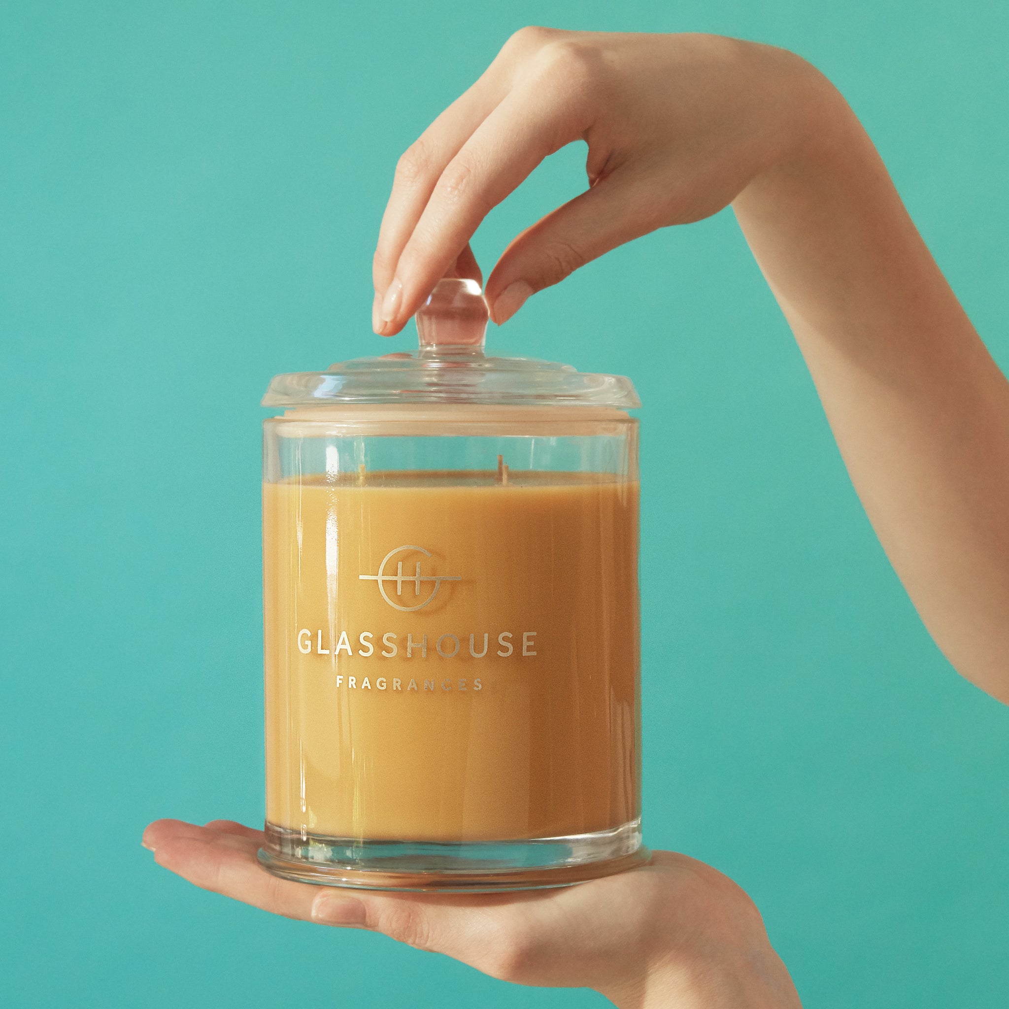 A Tahaa Affair  Vanilla Caramel Soy Candle held up by a pair of hands over a blue-green backdrop