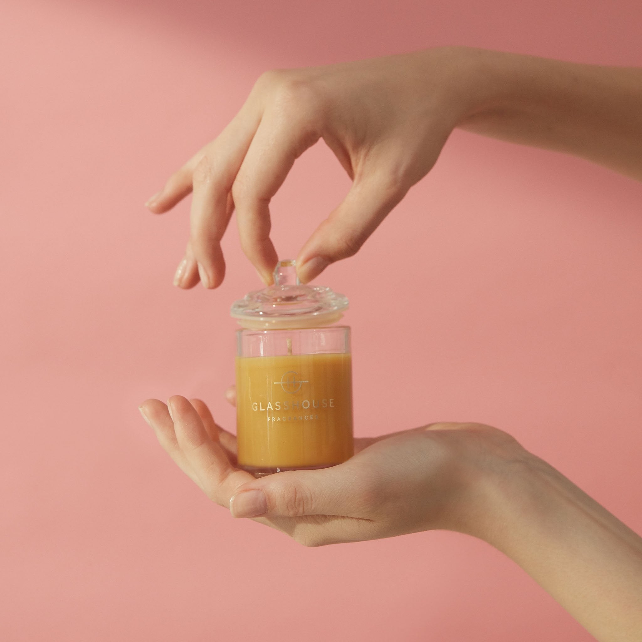 A Tahaa Affair 60g Vanilla Caramel Soy Candle held up  by a pair of hands over a peach-pink background